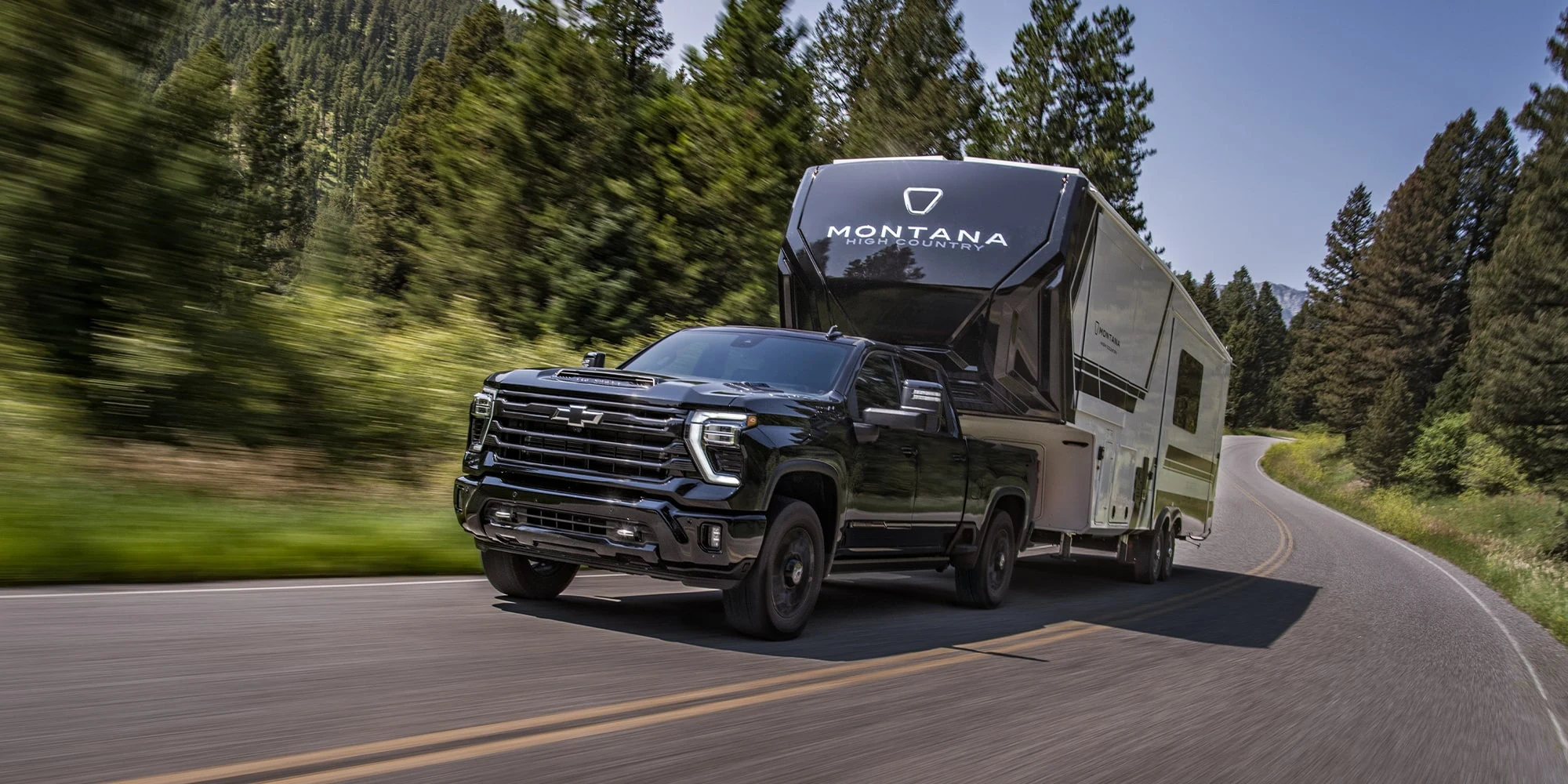Black Chevrolet Silverado HD towing a fifth-wheel camper on a forest road
