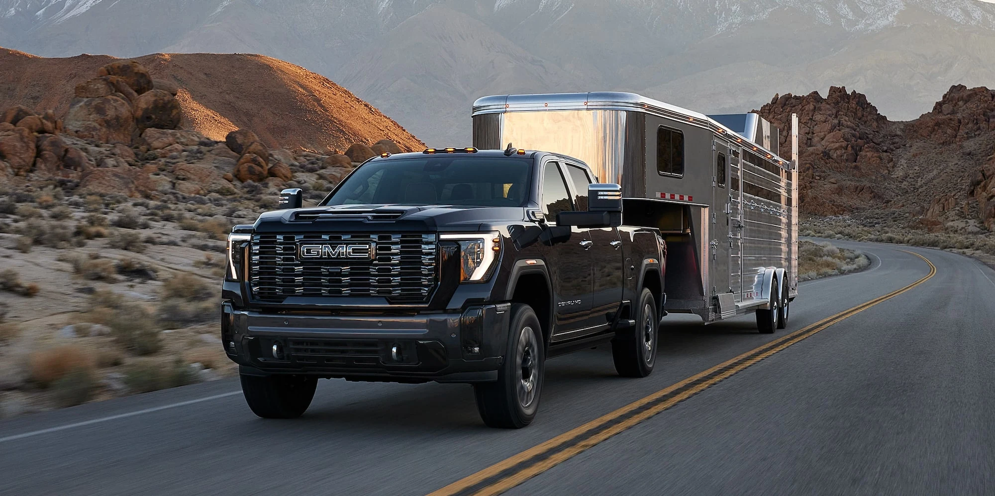 Dark GMC Sierra HD towing a horse trailer on a canyon road