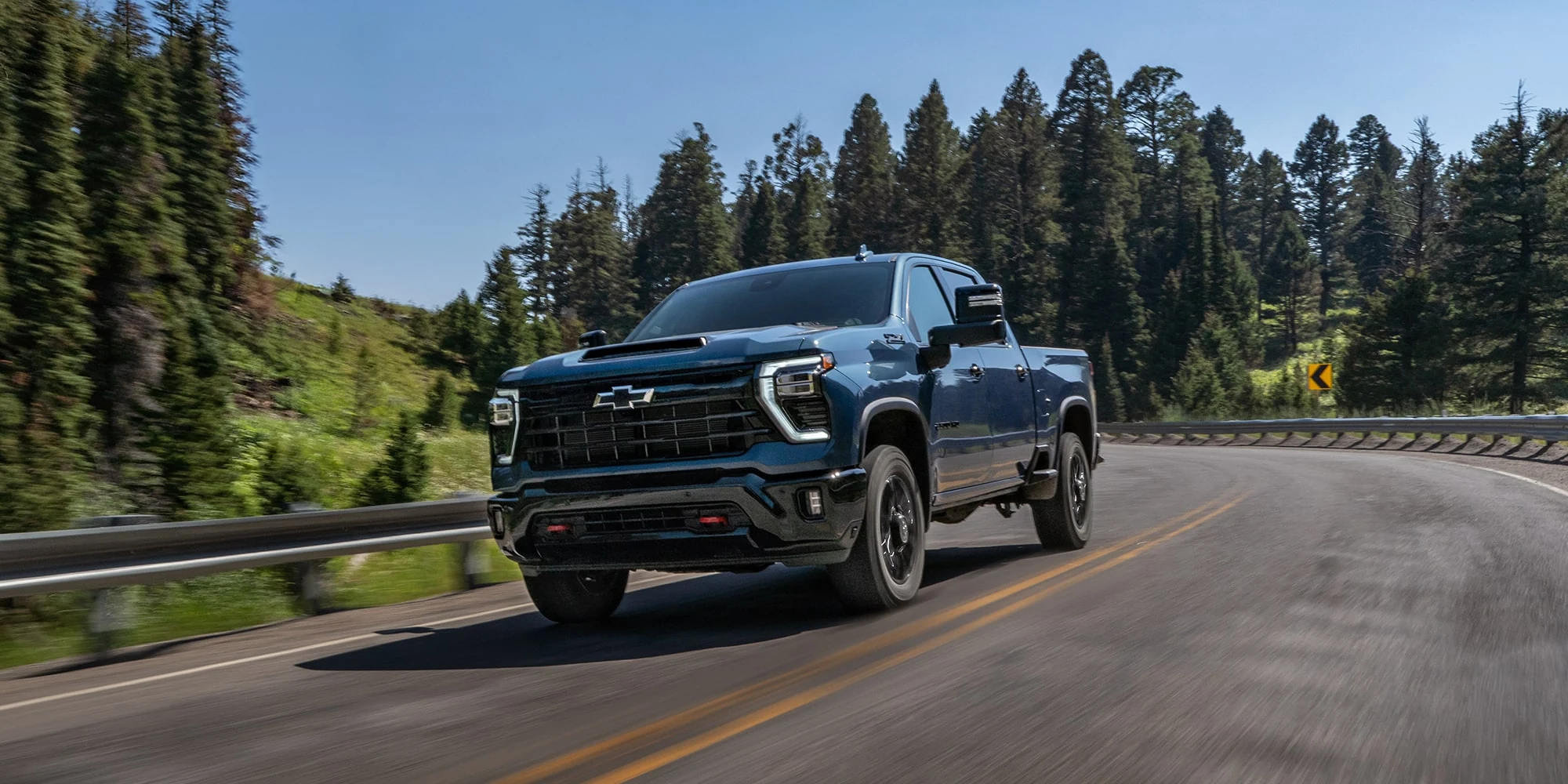 Black Chevrolet Silverado HD driving on a forest road, front three-quarter view