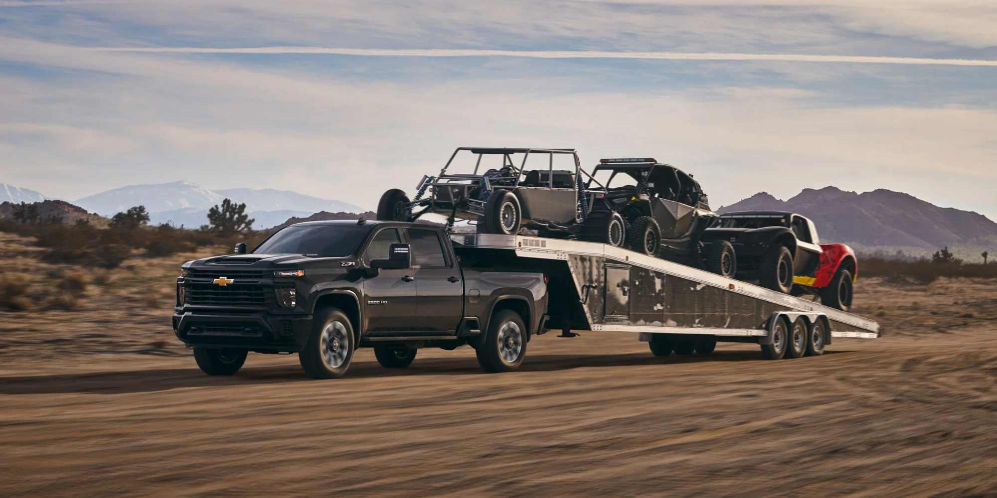 Gray Chevrolet Silverado HD towing a flatbed with off-road vehicles