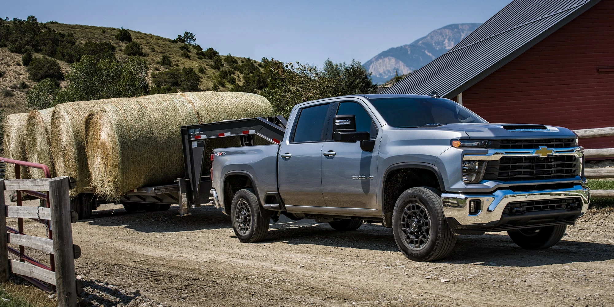 Silver Chevrolet Silverado HD towing a trailer loaded with hay beside a barn