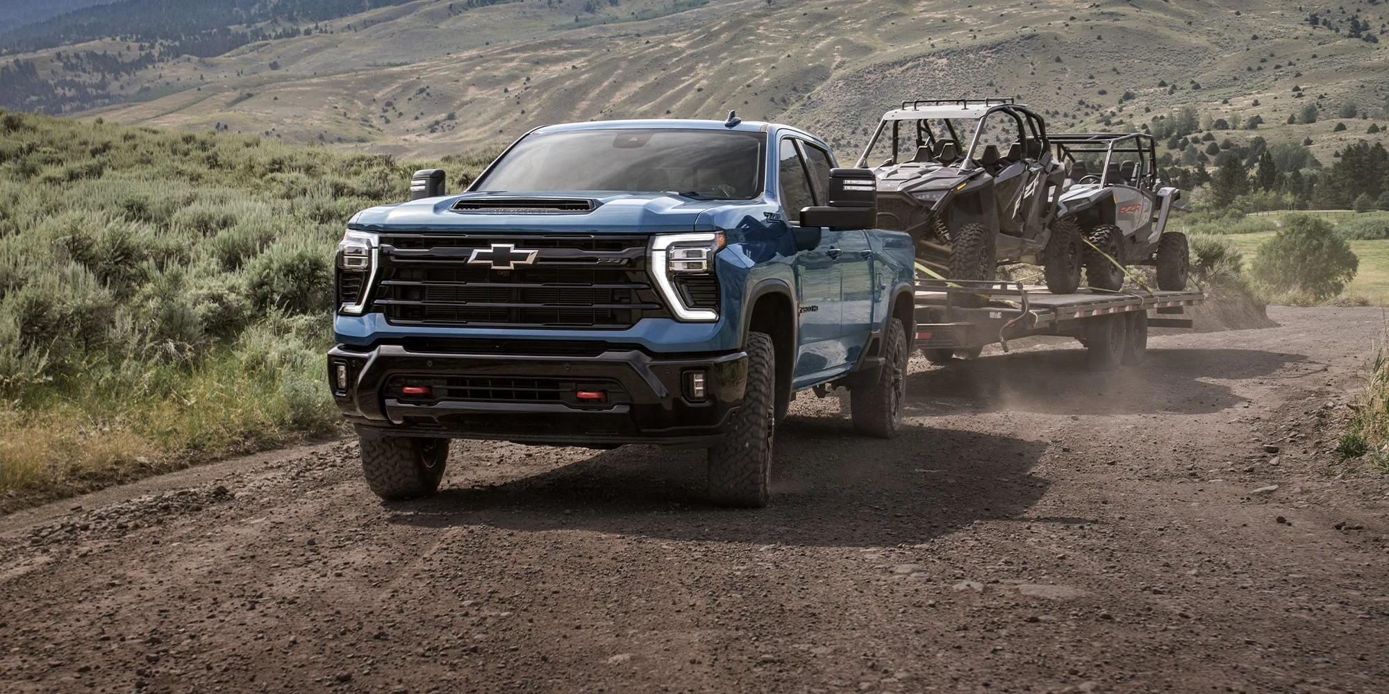 Blue Chevrolet Silverado HD towing a utility trailer on dirt