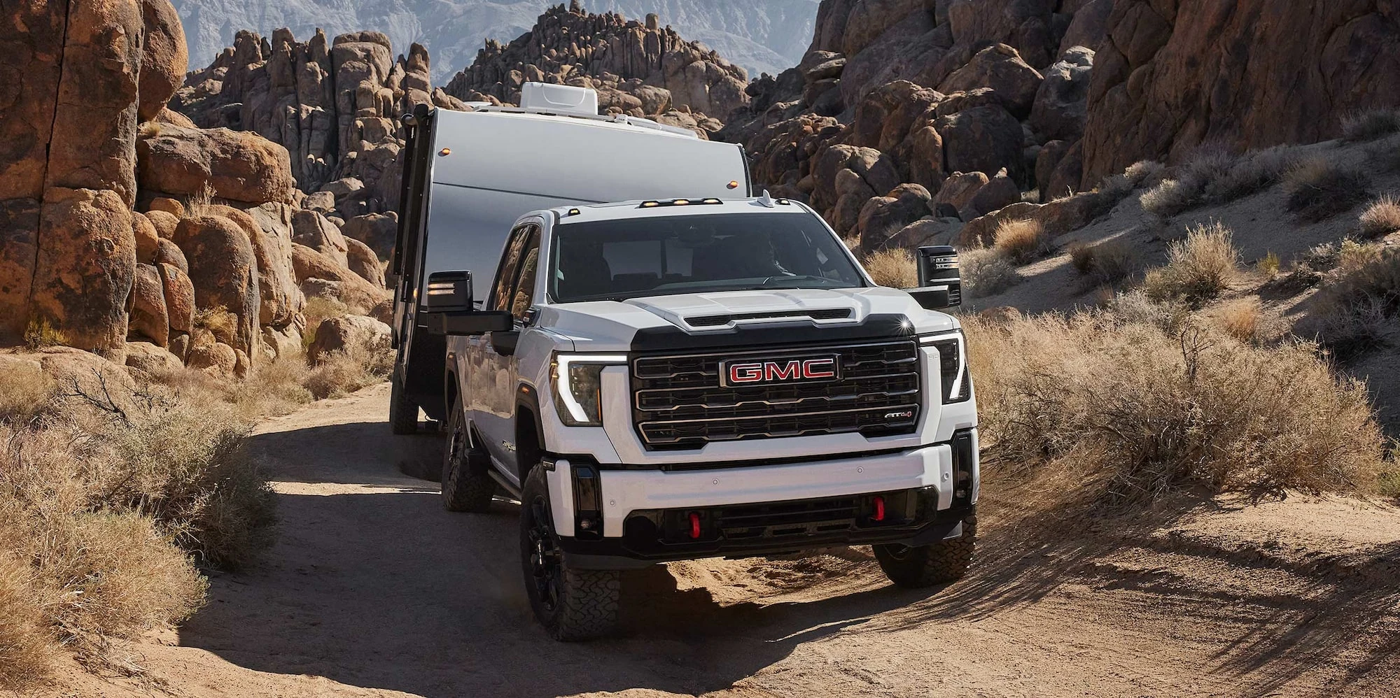 White GMC Sierra HD AT4X towing an adventure trailer over rocky ground