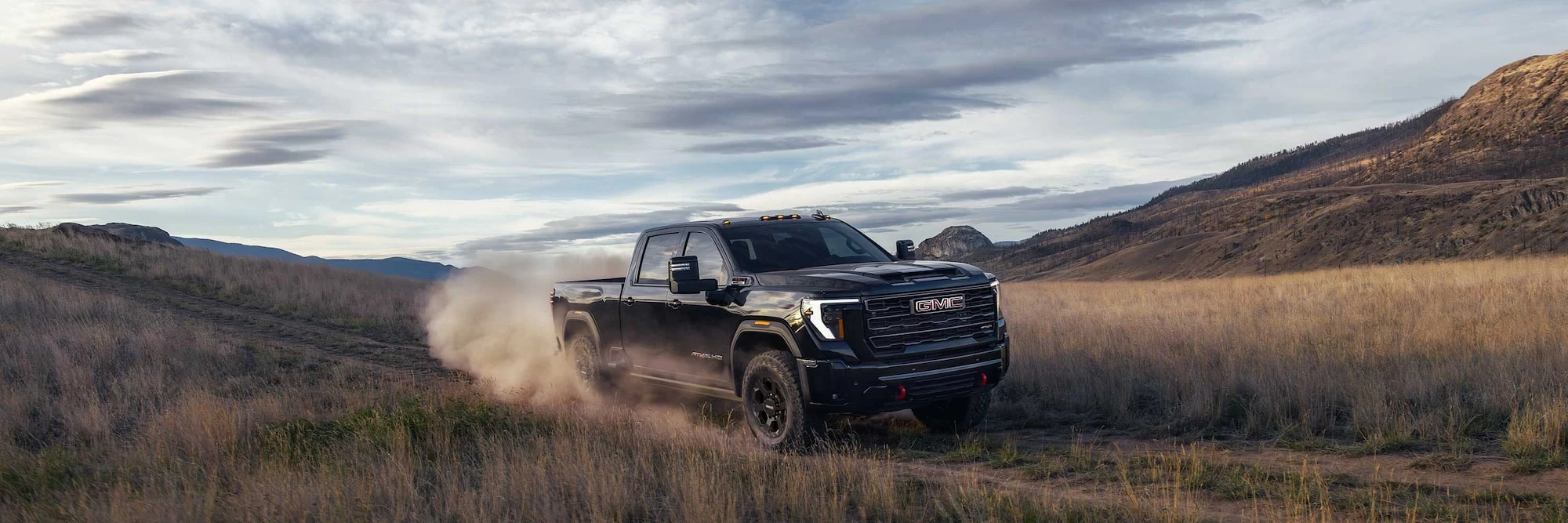 Black GMC Sierra HD driving through dust in an open landscape
